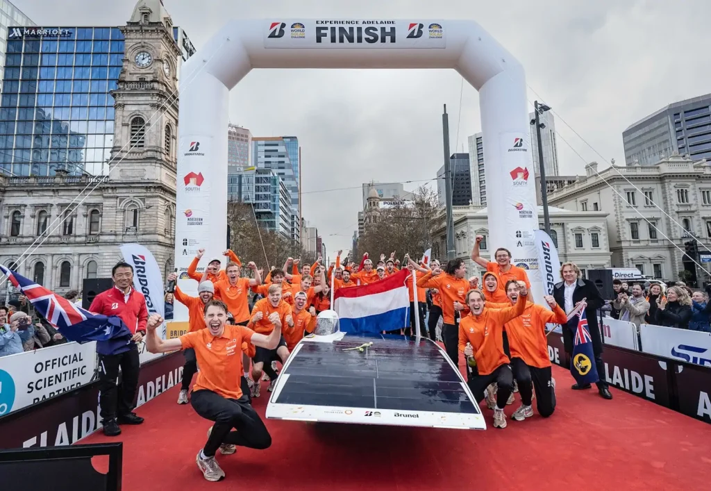 Team in orange clothing celebrates at the finish with a solar car