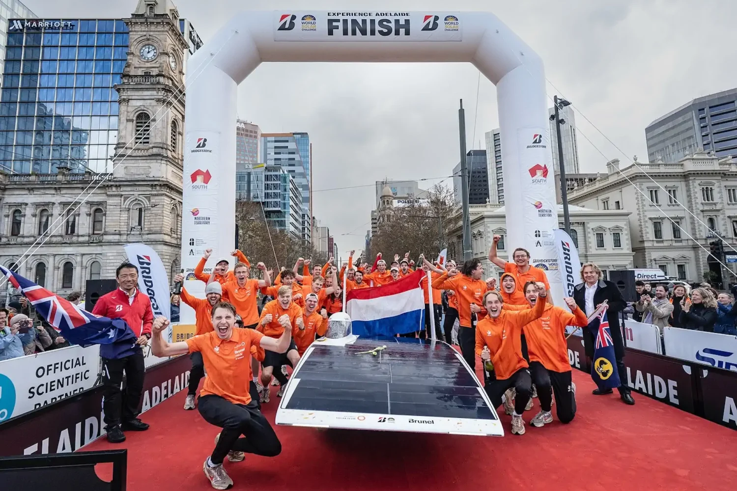 Team in orange clothing celebrates at the finish with a solar car