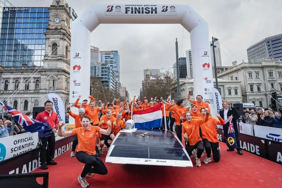 Team in orange clothing celebrates at the finish with a solar car