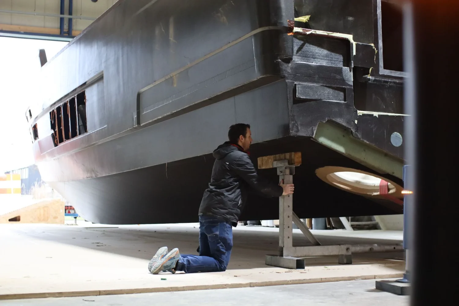 Employee kneeling beside the underside of a boat hull