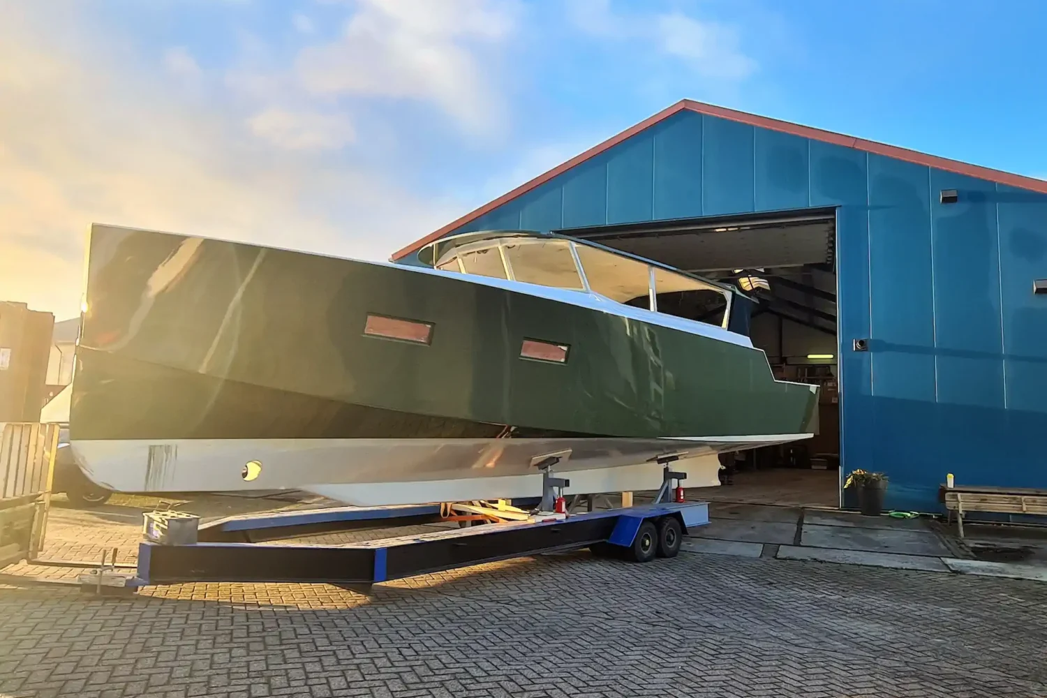 Light-coloured boat hull on a transport trolley in front of the workshop