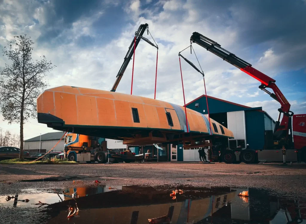 Orange boat hull being lifted by two cranes