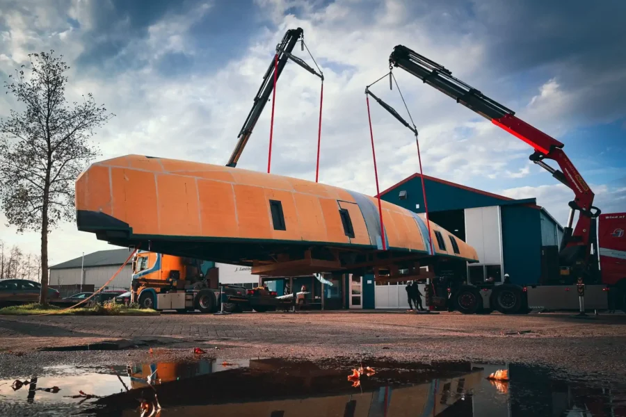 Orange boat hull being lifted by two cranes