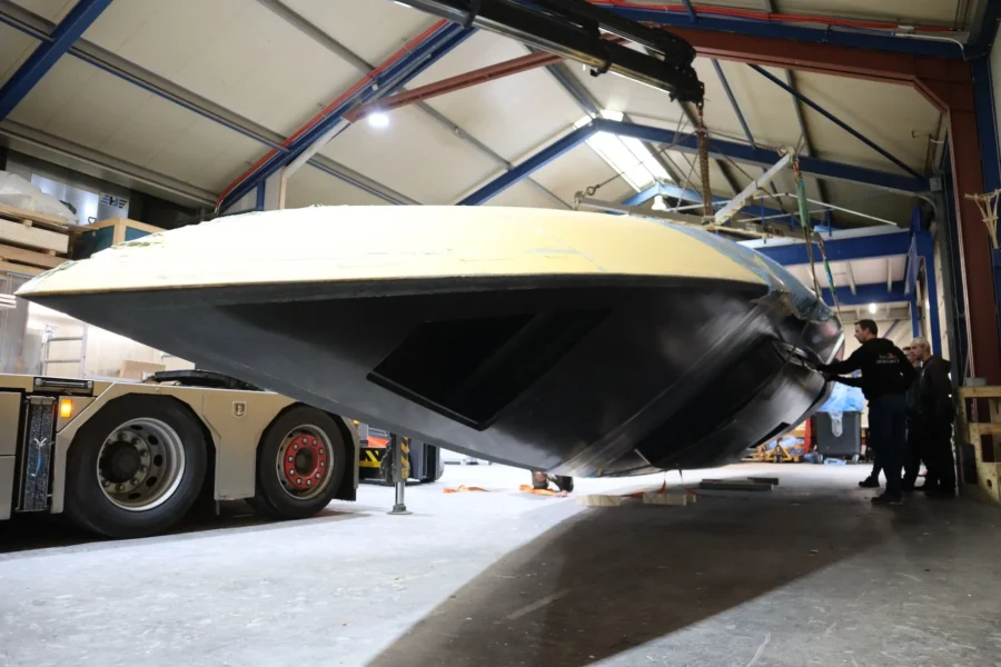 Boat hull suspended in lifting straps by the workshop door