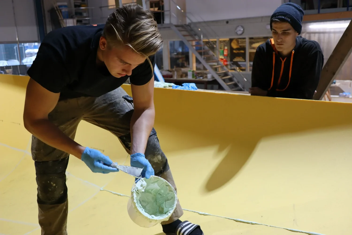 Employee wearing gloves applying material to a boat hull