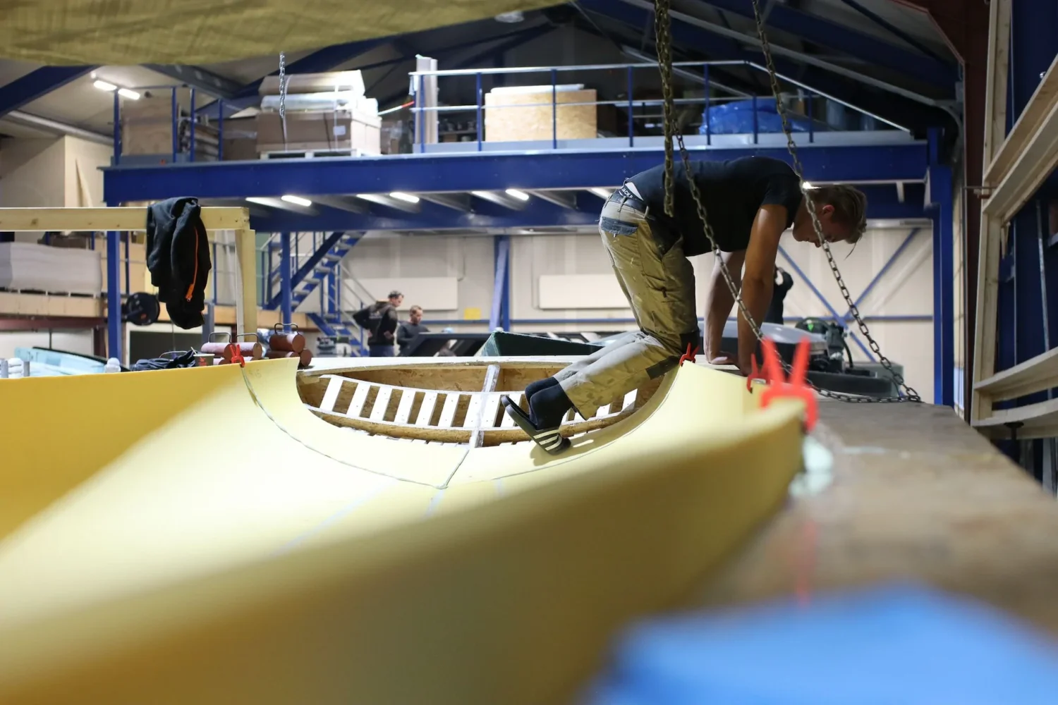 Employees working on a light-colored boat hull under construction