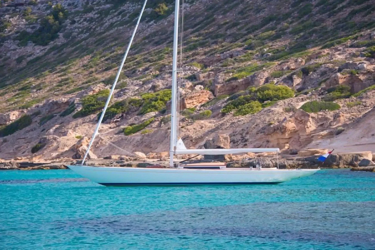 Sailing yacht anchored off a rocky coast