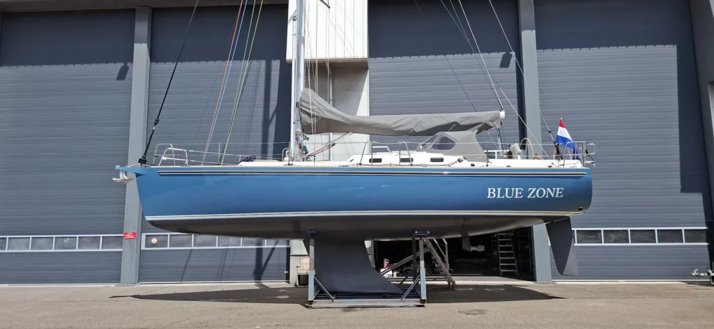 Blue sailing yacht Blue Zone on supports outside a workshop