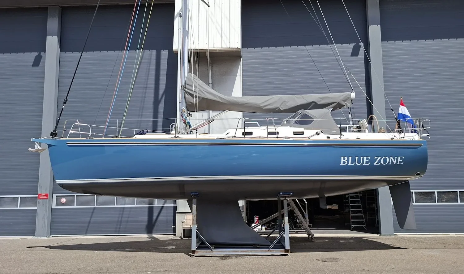 Blue sailing yacht Blue Zone on supports outside a workshop