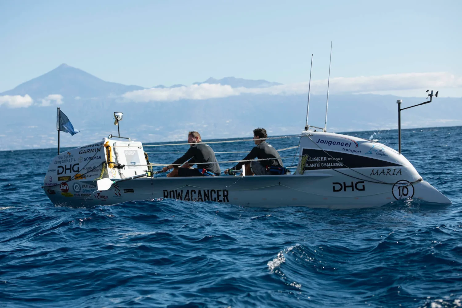 Two rowers at sea with mountains in the background