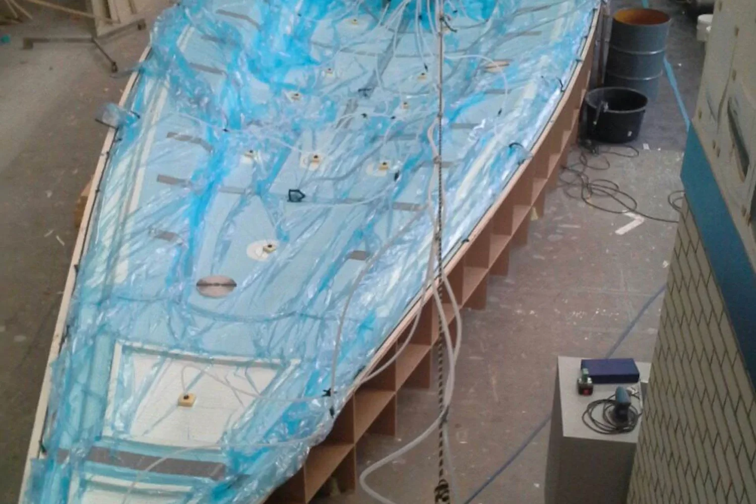 Boat hull beneath blue vacuum film in the workshop